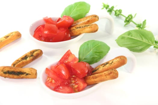 Grissini with tomato pieces and basil in appetizer spoons on white background