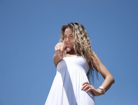 Portrait of the young woman pointing a finger against the blue sky