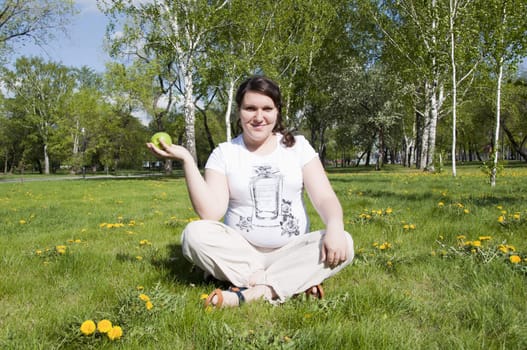 woman sitting on the grass in the park with an apple