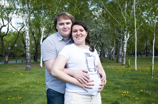 man hugs pregnant woman in the park