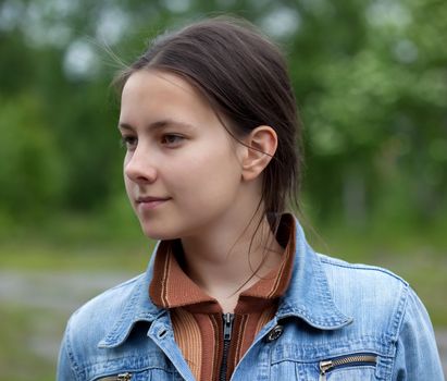 A girl in a denim jacket on a background of green foliage