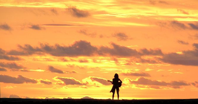 Woman standing on pier playing guitar to the beautiful sunset