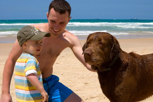 Happy father and son playing on beach with dog