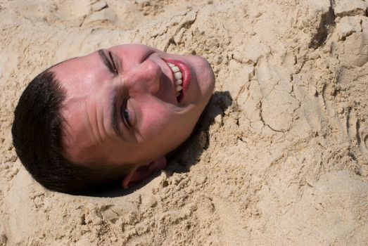 Happy smiling head of man protruding from the sand