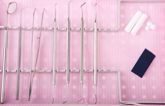 dentistry kit in a tray on pink bib (surgery instruments, articulation paper, cotton rolls and wools)