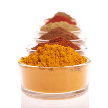 collection of indian spices (cumin, coriander, paprika, garam masala, curcuma, chili powder) on glass cups isolated on white background (shallow DOF, focus on first)