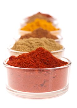 collection of indian spices (cumin, coriander, paprika, garam masala, curcuma, chili powder) on glass cups isolated on white background (shallow DOP, focus on first)