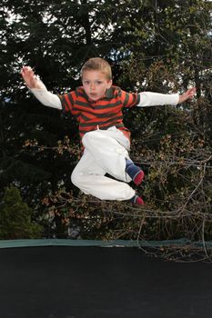 Blond boy jumping on his trampline in the garden