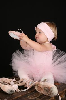 Blond toddler wearing a tutu holding Ballet shoes 