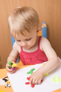 Baby girl moulding from plasticine at table