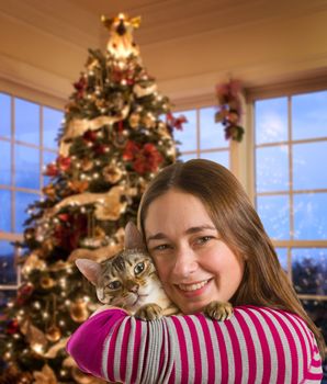 Young bengal kitten held on arm of young woman in front of brightly lit christmas tree