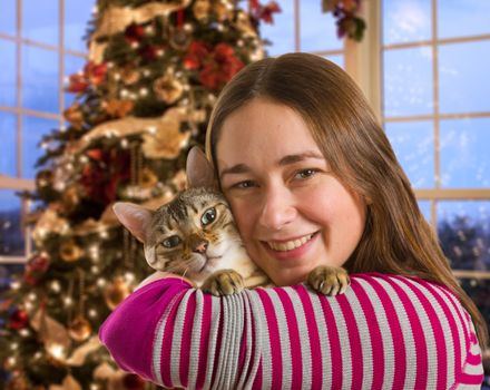 Young bengal kitten held on arm of young woman in front of brightly lit christmas tree