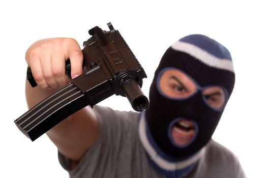 An angry looking man wearing a ski mask pointis a black automatic machine gun at the viewer. Shallow depth of field with sharpest focus on the gun.
