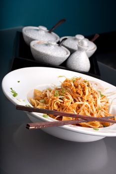 A Thai dish of crisy noodles and bean sprouts in a large white bowl with chop sticks.