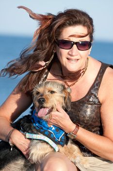 A middle aged woman by the ocean holding a cute mixed breed Beagle Yorkshire terrier dog also referred to as a Borkie.