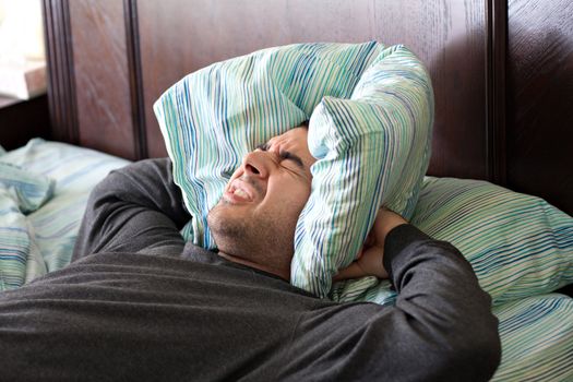 A man having trouble sleeping squeezes a pillow around his ears for some peace and quiet.