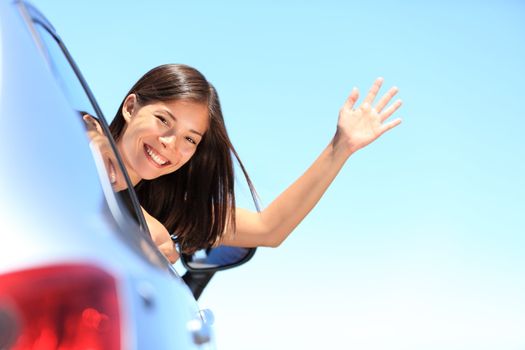 Car woman happy waving smiling at camera popping head out the window. New car, road trip vacation or drivers licence concept. Beautiful young mixed race Chinese Asian / white Caucasian woman.