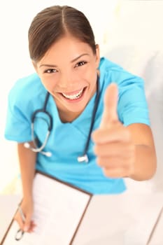 medical people. Woman nurse showing thumbs up success sign smiling happy and successful at camera. Beautiful young female nurse or young doctor with clipboard or positive medical record
