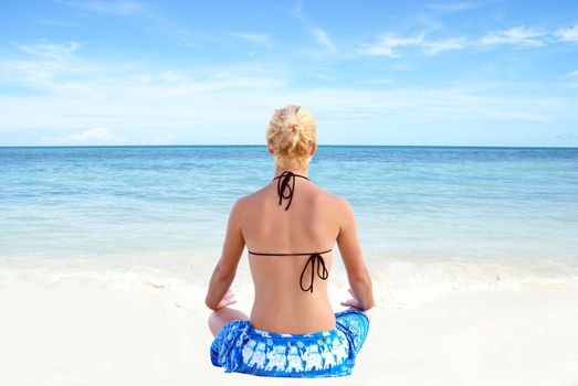A young woman meditates along the shores of the tropical ocean.