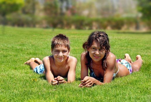 smiling boy and girl lying on green grass outdoors at summer