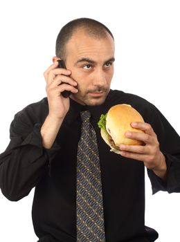 Young businessman eating hamburger, talking by cellphone