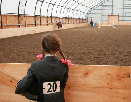 a young lady, helmet under her arm, waiting to be called to compete in a horse show