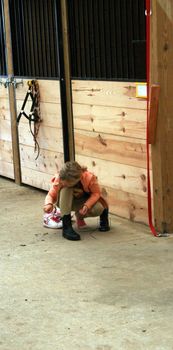 just before the horse show, a young equestrian ties her boots in the stable