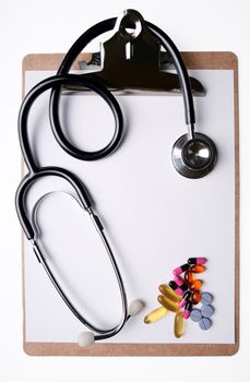 Stethoscope and medicine on clipboard with blank sheet of paper