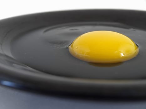 A raw egg cracked on a black plate. Studio isolation.