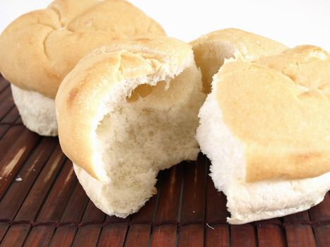 Fresh rolls of bread on a bamboo mat. Broken roll at front. Studio isolated over white.