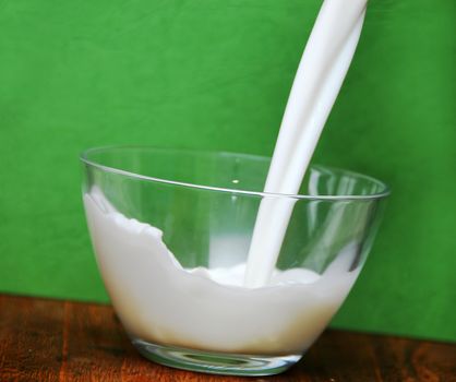 pouring milk in glass bowl over green background
