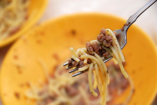 spaghetti mixed with minced meat of fork over yellow plate