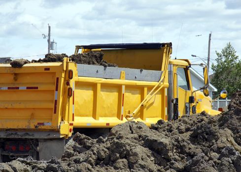 Bright yellow dump truck being filled at big construction site and parked right beside heap of dirt.