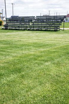 Before the big game: Empty wood bleachers for the fans and parents of the local soccer or football team with field grass in the forefront as copy space.