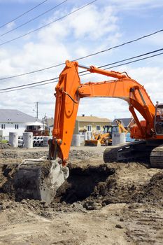 Bright orange mechanical digger removing dirt to install sewage and water line for a new neighborhood in rural North America.