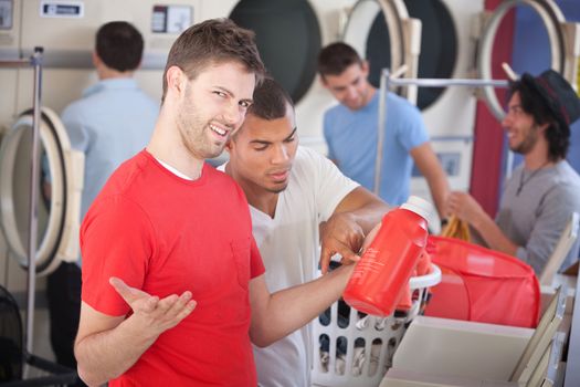 Young man and his friend struggle with soap instructions in the laundromat