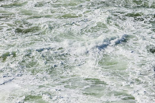 Foam on the water made by turning ship giving a light green color to the water