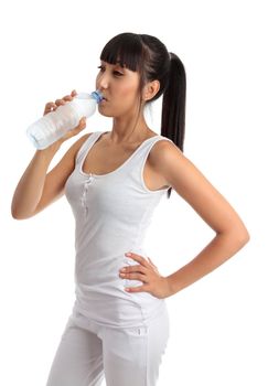 A young beautiful girl wearing white gym clothes is drinking refreshing water from a clear plastic bottle. White background.