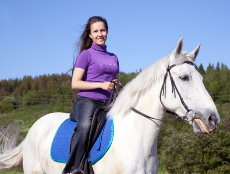 Girl on a white horse against the backdrop of the forest on a clear day