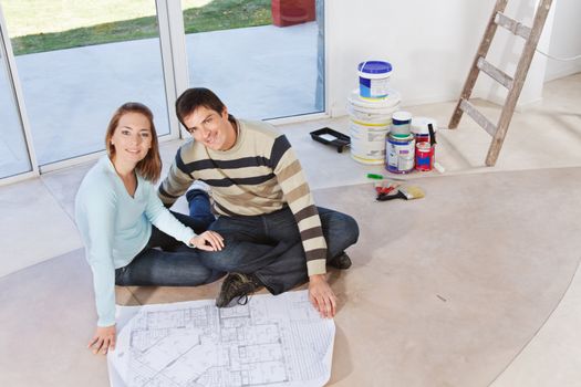 Happy young couple sitting together with blueprint and color buckets in the background