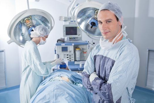 Smiling male doctor with arms crossed in operating room