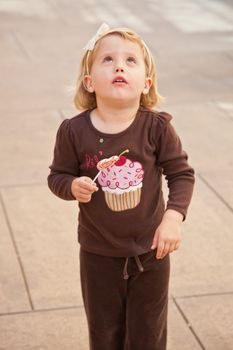 Cute little European toddler girl having fun eating heart shaped lollypop