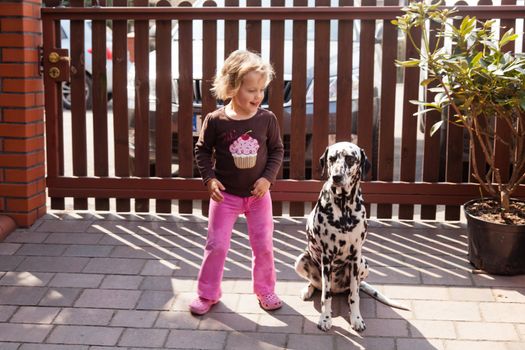 Little girl playing with dalmatian in a garden.