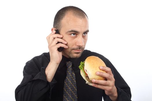 Young businessman eating hamburger, talking by cellphone