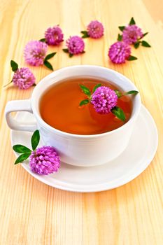 Herbal tea with clover in the white porcelain cup, clover flowers on a wooden board