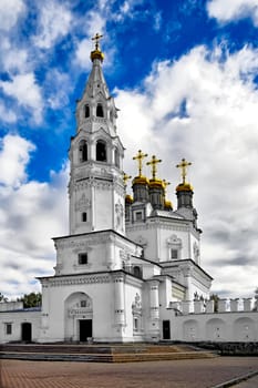 White Stone Holy Trinity church tower with gold baths and crosses against the blue sky, white clouds (Verhoturie city of Sverdlovsk Region)