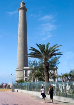 The Lighthouse of Maspalomas Gran Canaria from the promenade with palm trees and a blue sky