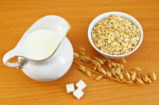 Milk in a milkman, oatmeal in a bowl, three lumps of sugar, stem of oat on background a wooden table top