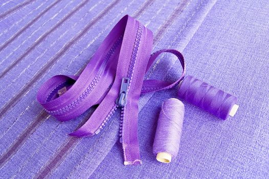 Locking zipper and two reels of thread on the purple plain and striped fabrics