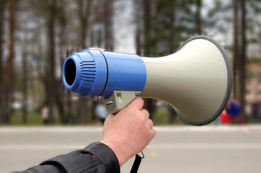 Blue with gray megaphone in hand, men in the background of trees and roads